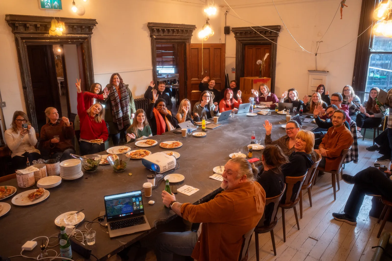 The whole RKH team waving from around one long table at a staff meeting